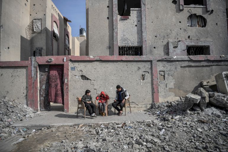 فلسطينيون يجلسون أمام أنقاض منزلهم الذي دمره الاحتلال الإسرائيلي في غزة